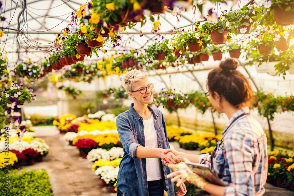 Florist holding tablet and shaking hands with happy customer. Greenhouse interior. Florist holding tablet and shaking hands with happy customer. Greenhouse interior.