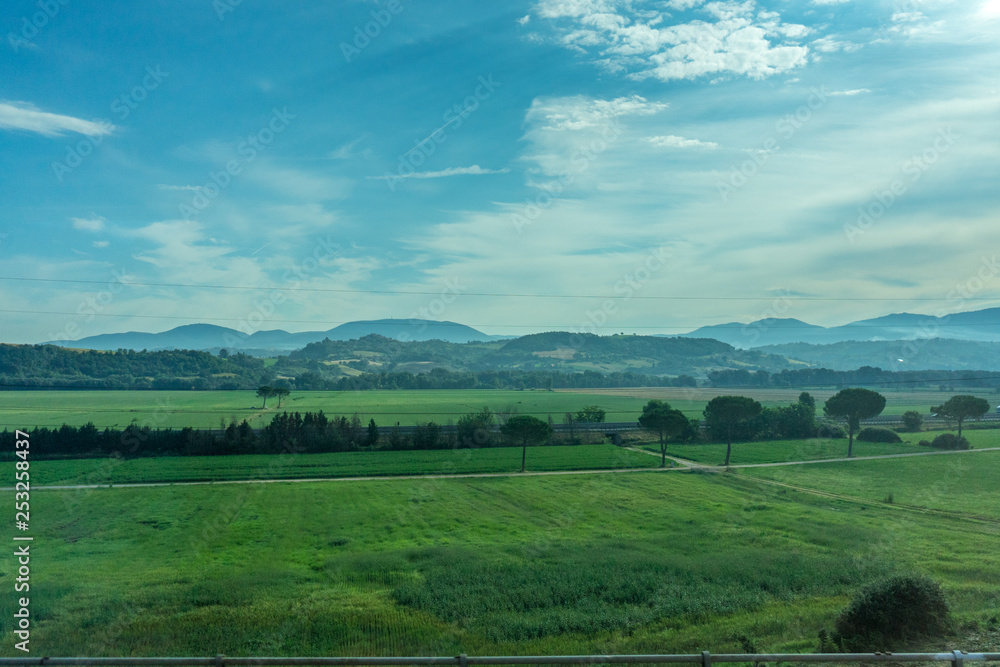 Italy, Rome to Florence train, a large green field with a mountain in the background Italy, Rome to Florence train, a large green field with a mountain in the background
