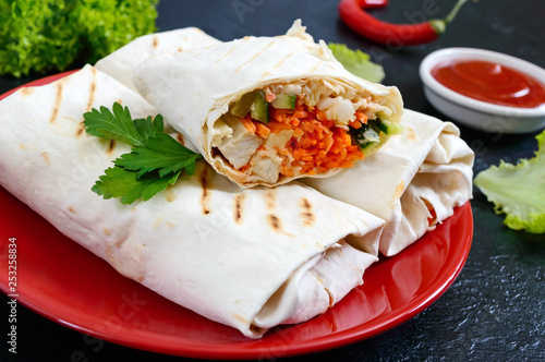 Delicious shawarma sandwich on a black background. Burritos wraps with grilled chicken and vegetables, greens. Fajitas, pita bread. Traditional Middle Eastern appetizer. Mexican cuisine