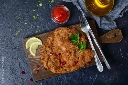 Large Viennese schnitzel on a black background. Meat dish. Top view, flat lay. photo