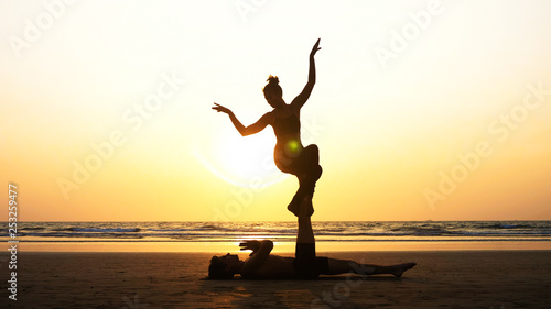 Silhouette of fit sporty couple practicing acrobatic yoga with partner together on the beach.