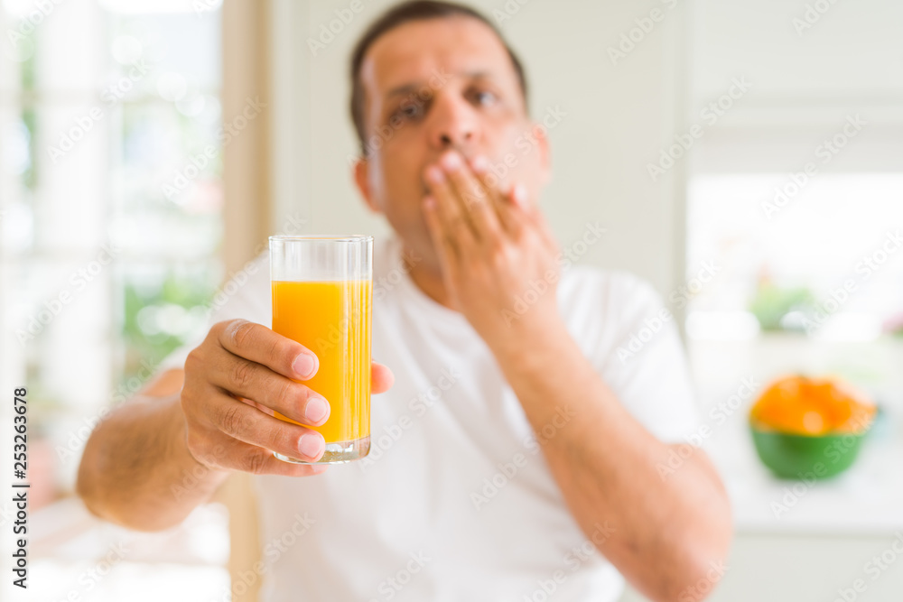 Middle age man drinking a glass of orange juice at home cover mouth with hand shocked with shame for mistake, expression of fear, scared in silence, secret concept Middle age man drinking a glass of orange juice at home cover mouth with hand shocked with shame for mistake, expression of fear, scared in silence, secret concept