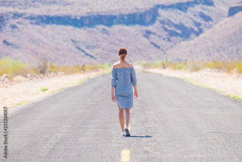Young woman walking on an endless straight empty road in the middle of nowhere on the Route 66 road. Backpackers, visionary, entrepreneur, adventure concepts.