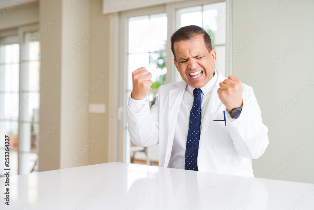 Middle age doctor man wearing medical coat at the clinic very happy and excited doing winner gesture with arms raised, smiling and screaming for success. Celebration concept. Middle age doctor man wearing medical coat at the clinic very happy and excited doing winner gesture with arms raised, smiling and screaming for success. Celebration concept.