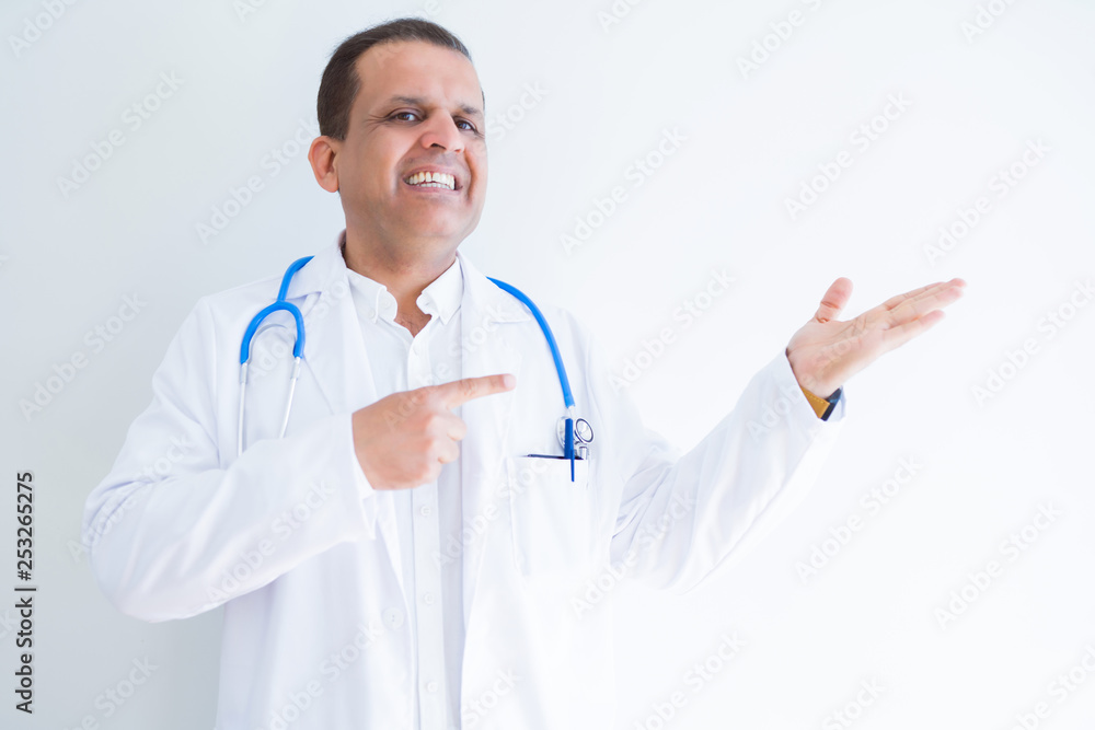 Middle age doctor man wearing stethoscope and medical coat over white background amazed and smiling to the camera while presenting with hand and pointing with finger. Middle age doctor man wearing stethoscope and medical coat over white background amazed and smiling to the camera while presenting with hand and pointing with finger.