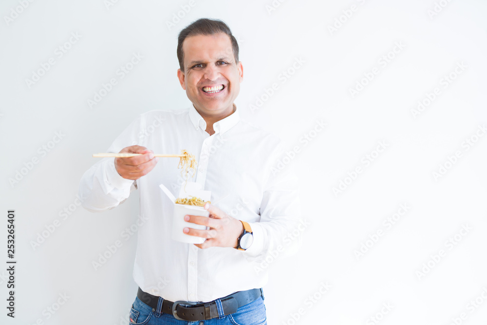 Middle age man eating asian noodles from take away carton with a happy face standing and smiling with a confident smile showing teeth Middle age man eating asian noodles from take away carton with a happy face standing and smiling with a confident smile showing teeth