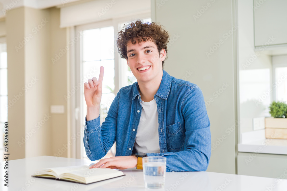 Young man reading a book at home surprised with an idea or question pointing finger with happy face, number one