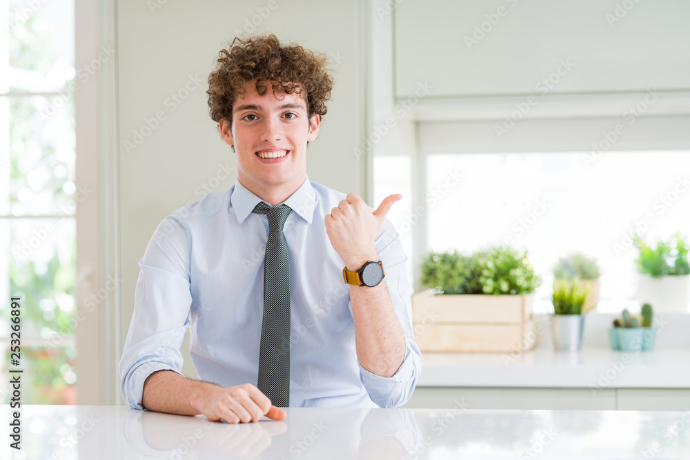 Young business man wearing a tie smiling with happy face looking and pointing to the side with thumb up.