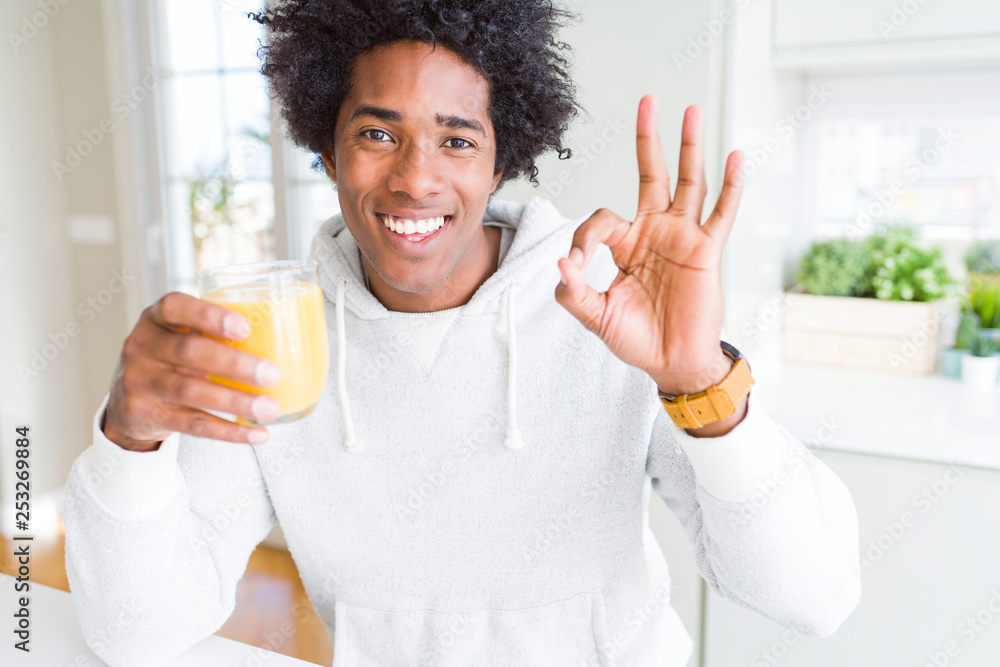 African American man holding and drinking glass of orange juice doing ok sign with fingers, excellent symbol African American man holding and drinking glass of orange juice doing ok sign with fingers, excellent symbol