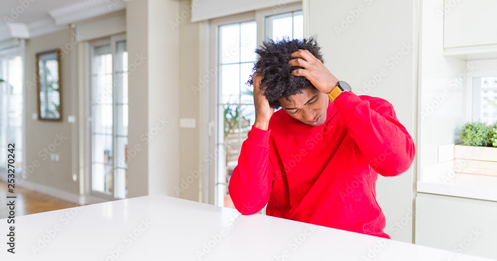 African American man wearing casual red sweatshirt suffering from headache desperate and stressed because pain and migraine. Hands on head. African American man wearing casual red sweatshirt suffering from headache desperate and stressed because pain and migraine. Hands on head.
