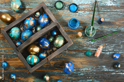 Painted colored Easter eggs in dark wooden box on dark wooden background. Boho stile.