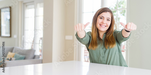 Beautiful young woman at home approving doing positive gesture with hand  thumbs up smiling and happy for success. Looking at the camera  winner gesture.