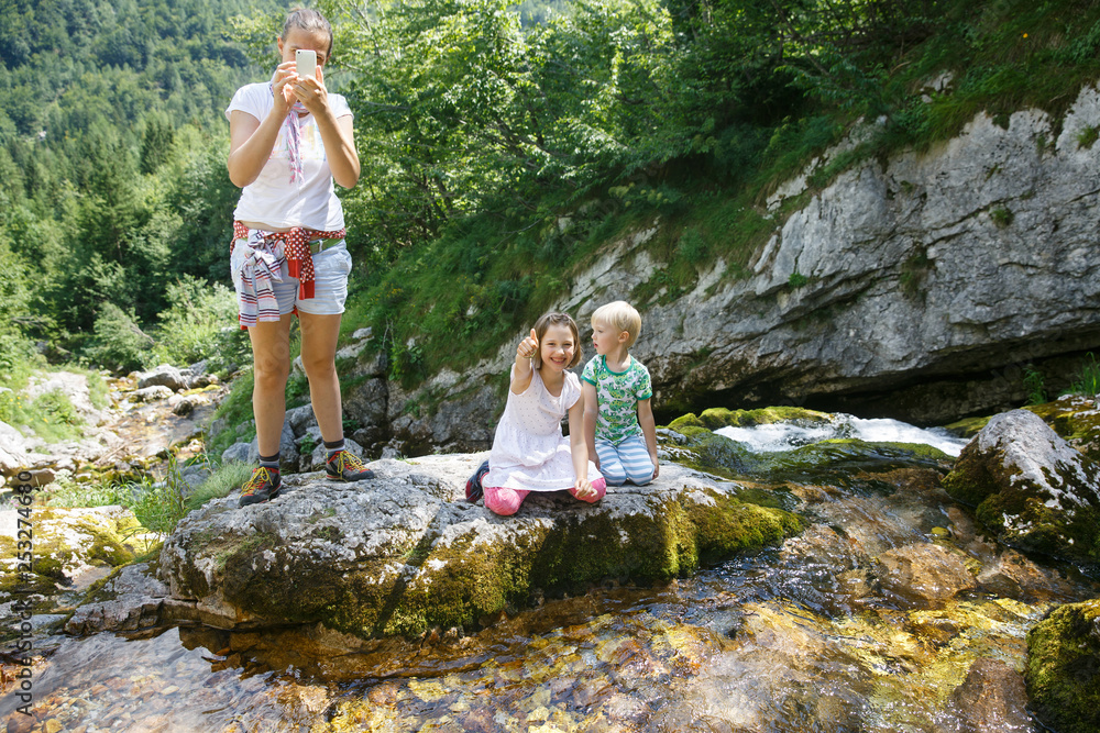 Mother taking a snapshot on a family trip with kids by a mountain stream.