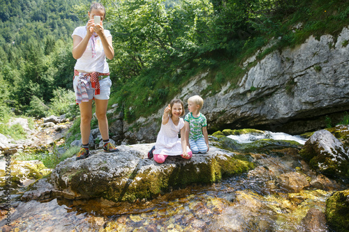Obraz na płótnie Mother taking a snapshot on a family trip with kids by a mountain stream. w salonie