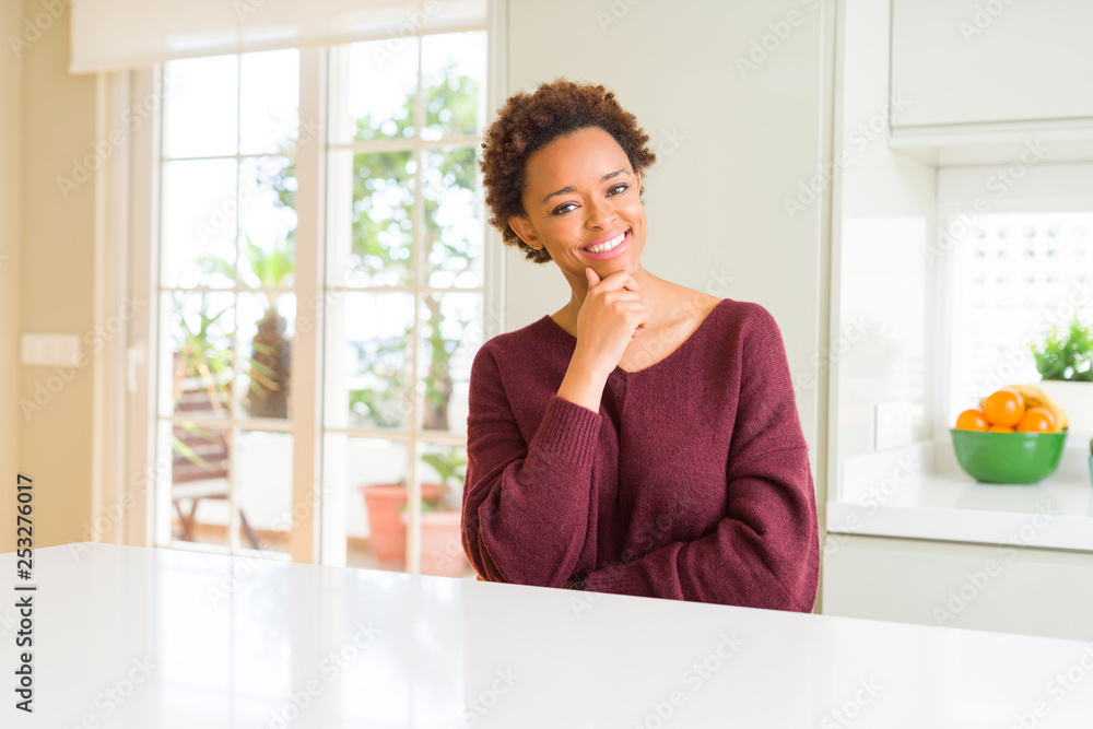 Young beautiful african american woman at home looking confident at the camera with smile with crossed arms and hand raised on chin. Thinking positive. Young beautiful african american woman at home looking confident at the camera with smile with crossed arms and hand raised on chin. Thinking positive.