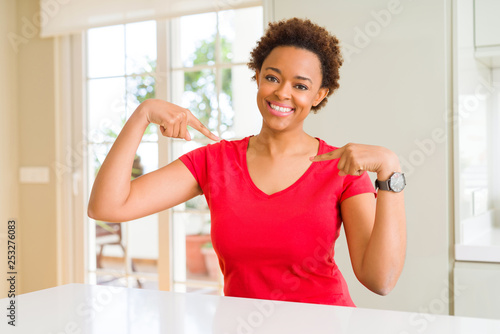 Young beautiful african american woman at home looking confident with smile on face  pointing oneself with fingers proud and happy.