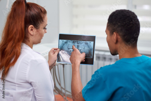 Caucasian female dentist explaining to african male rookie x-ray