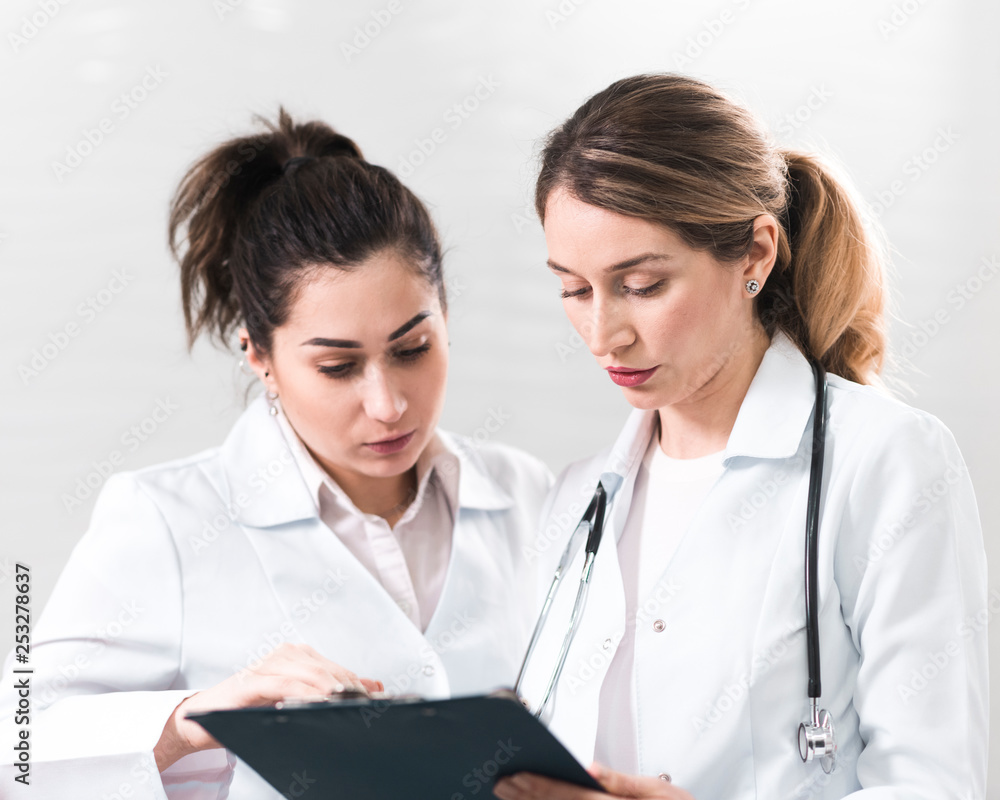 Two female assistants dressed in white coats talking to each other in the dentistry center Two female assistants dressed in white coats talking to each other in the dentistry center