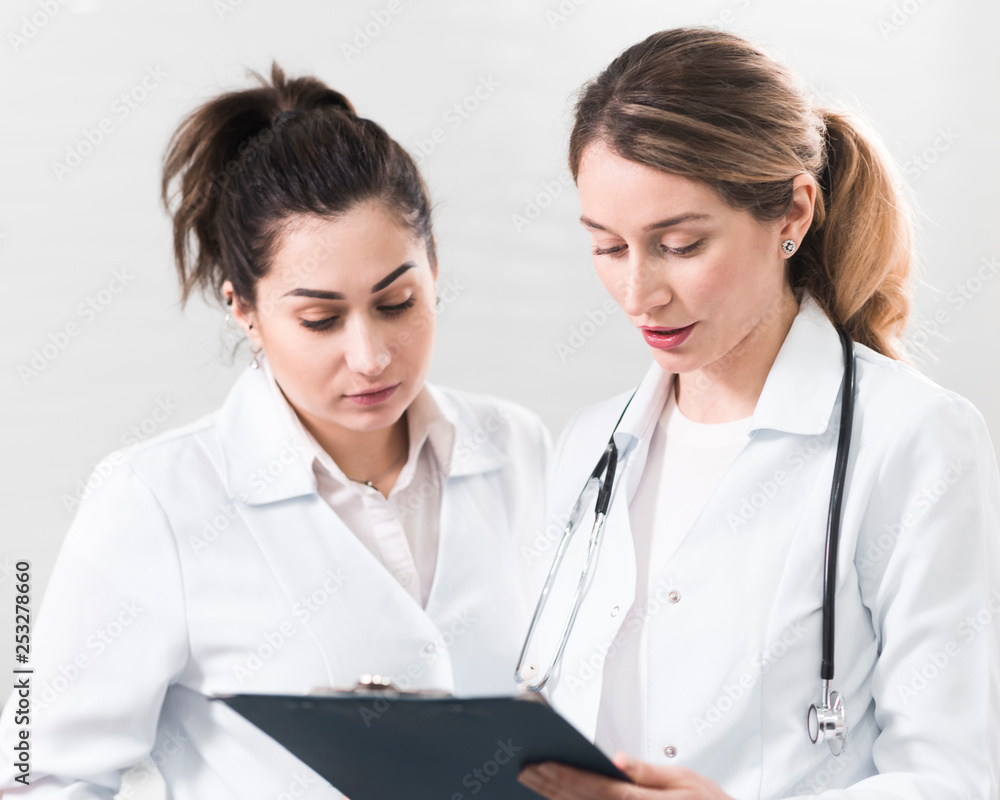 Two female assistants dressed in white coats talking to each other in the dentistry center Two female assistants dressed in white coats talking to each other in the dentistry center