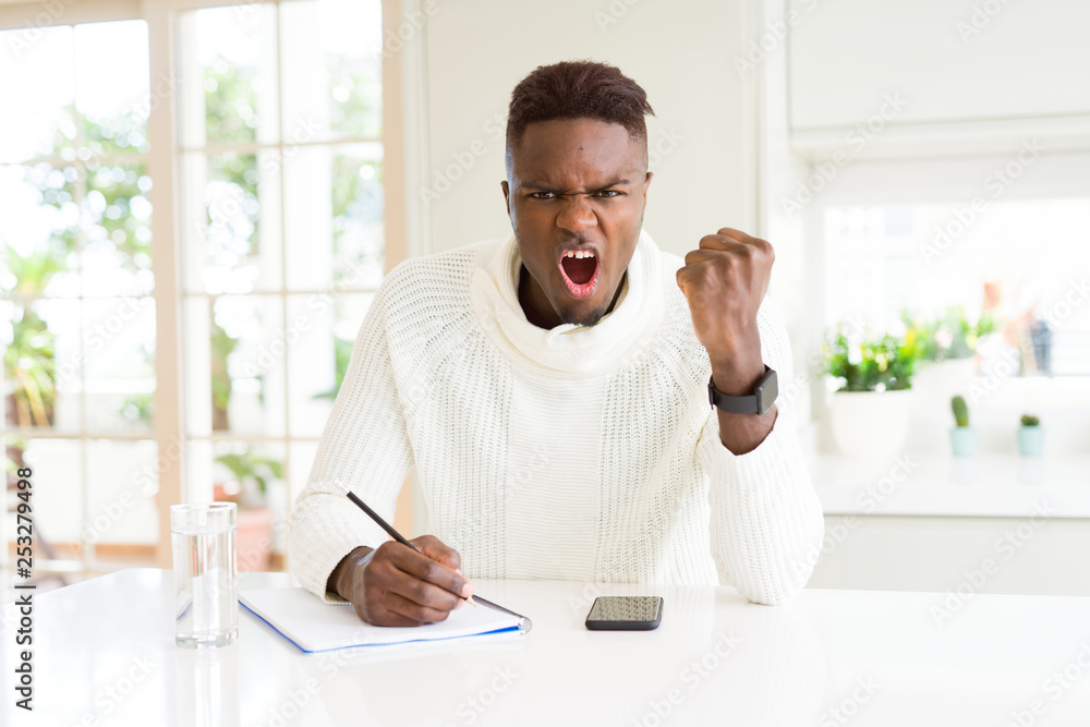 African american student man writing on a paper using a pencil annoyed and frustrated shouting with anger, crazy and yelling with raised hand, anger concept African american student man writing on a paper using a pencil annoyed and frustrated shouting with anger, crazy and yelling with raised hand, anger concept