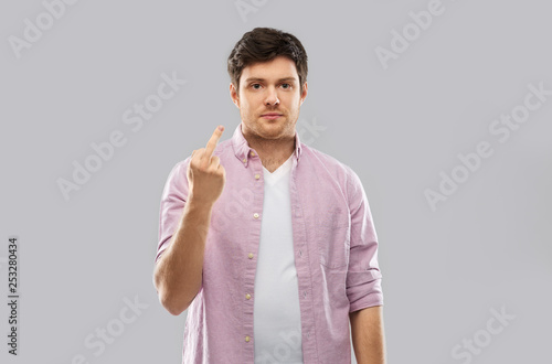 people concept - young man showing middle finger over grey background