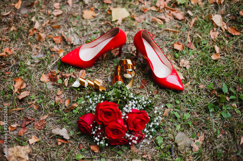 Red shoes and wedding bouquet of red roses on the grass. Bridal details
