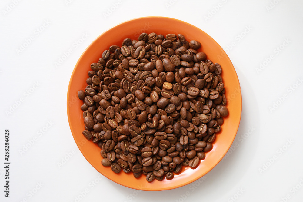 Orange saucer with coffee beans on white table Orange saucer with coffee beans on white table