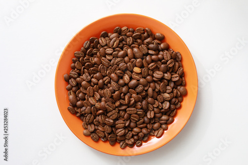Orange saucer with coffee beans on white table