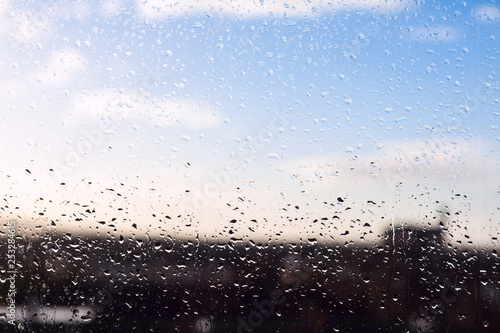 Blurred urban background with blue cloudy sky behind wet window