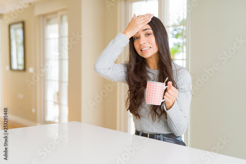 Young woman drinking a cup of coffee stressed with hand on head  shocked with shame and surprise face  angry and frustrated. Fear and upset for mistake.