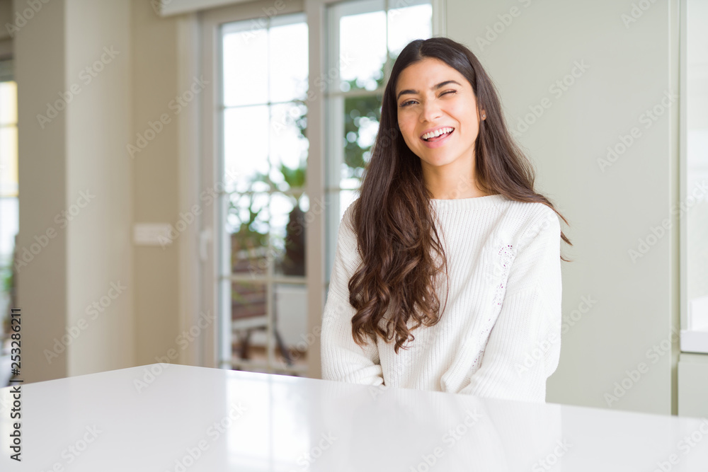 Young beautiful woman at home on white table winking looking at the camera with sexy expression, cheerful and happy face. Young beautiful woman at home on white table winking looking at the camera with sexy expression, cheerful and happy face.