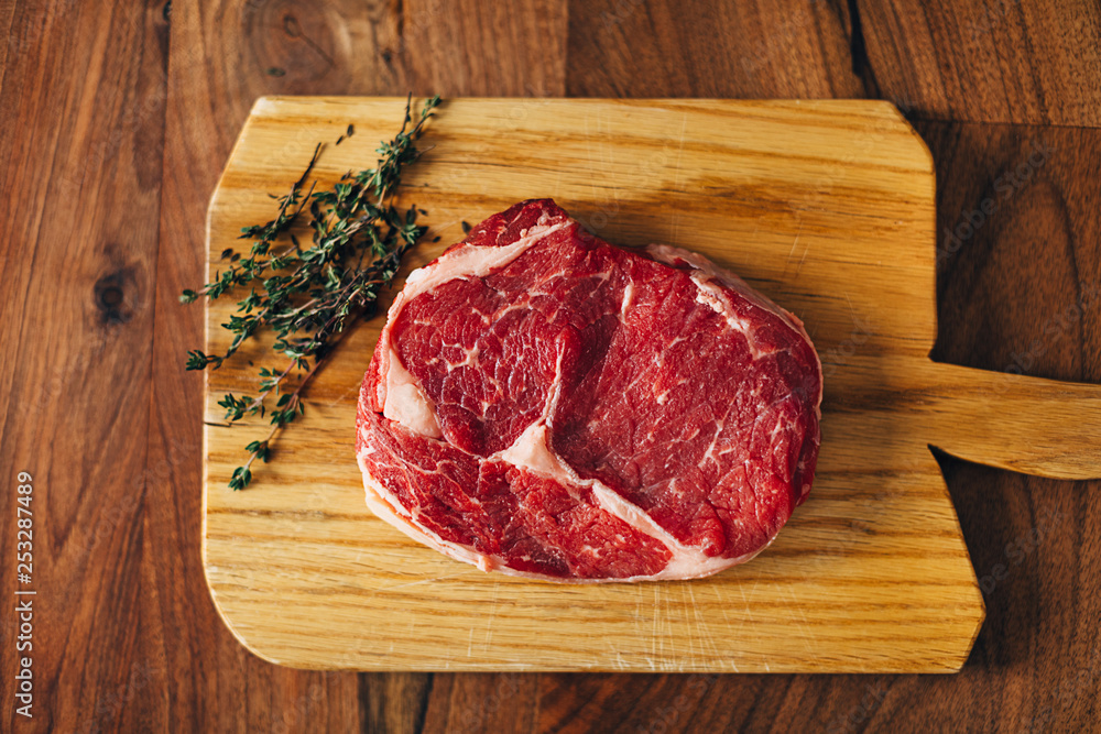 Overhead shot of ribeye steak resting on a wooden board in the kitchen with fresh thyme. Top shot Overhead shot of ribeye steak resting on a wooden board in the kitchen with fresh thyme. Top shot