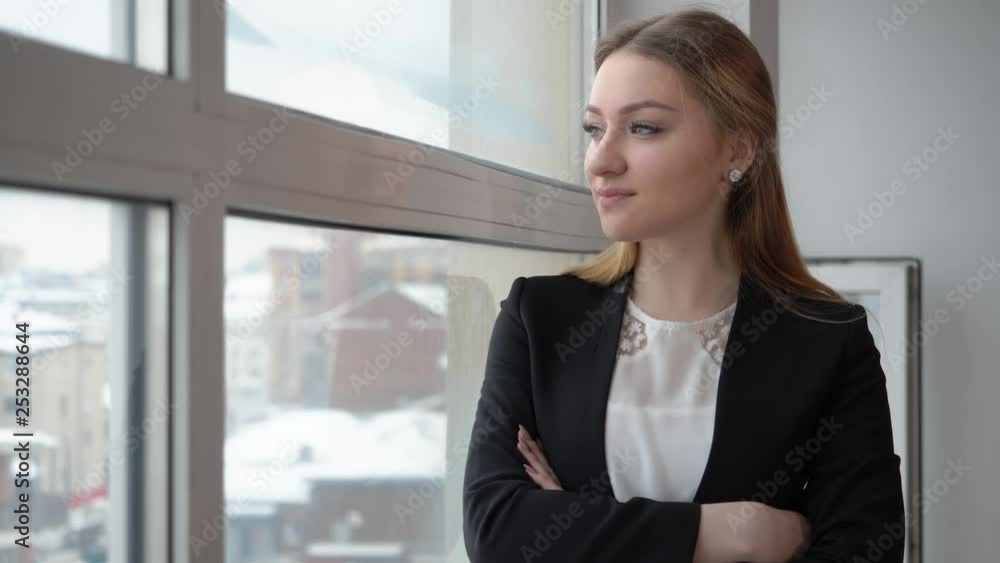 Serious businesswoman in black suit looking to window in modern office. Impatient woman standing near window in business office. Business people concept Serious businesswoman in black suit looking to window in modern office. Impatient woman standing near window in business office. Business people concept
