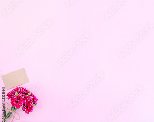 May mothers day idea concept photography - Beautiful blooming carnations tied by bow with kraft text card isolated on bright modern table, copy space, flat lay, top view, mock up © RomixImage