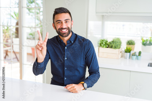 Handsome hispanic man smiling with happy face winking at the camera doing victory sign. Number two.