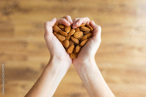 Young woman hands forming heart shape holding almonds nuts at home.