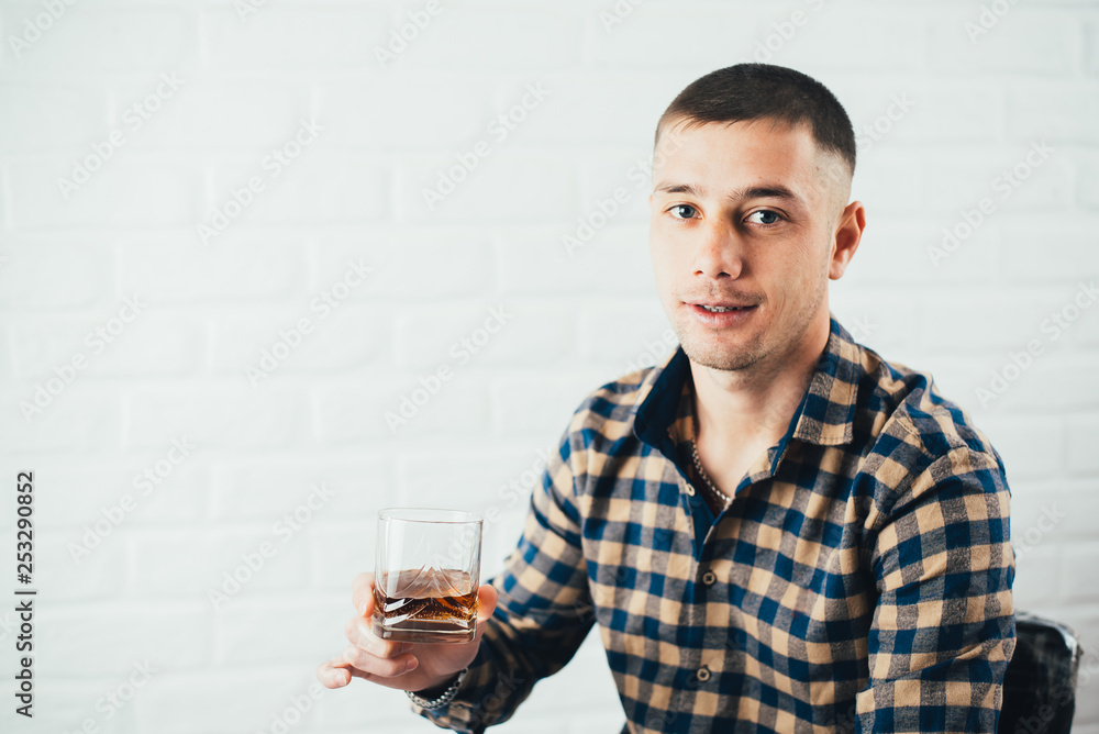 Young businessman with a glass of whiskey and a white brick wall Young businessman with a glass of whiskey and a white brick wall