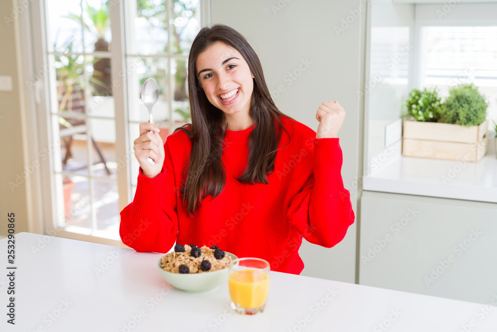 Beautiful young woman having healthy cereals and berries for breakfast screaming proud and celebrating victory and success very excited, cheering emotion Beautiful young woman having healthy cereals and berries for breakfast screaming proud and celebrating victory and success very excited, cheering emotion