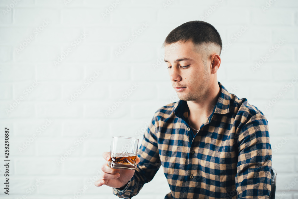Young businessman with a glass of whiskey and a white brick wall Young businessman with a glass of whiskey and a white brick wall