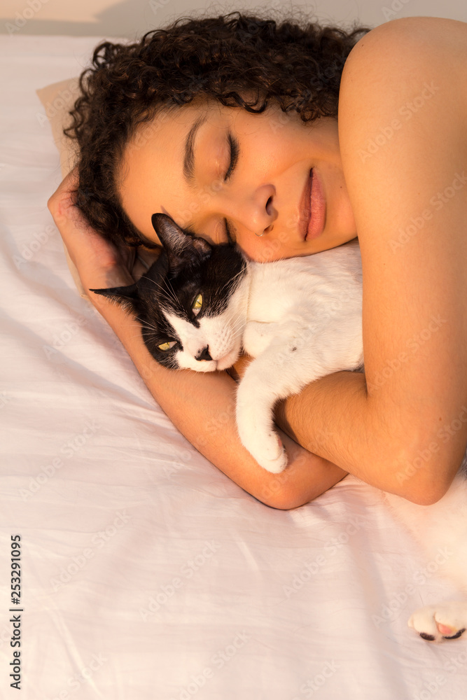 Portrait of woman with curly hair sleeping with her black and white cat in bed. Concept of love to animals, pets, care, tranquility, peace. Portrait of woman with curly hair sleeping with her black and white cat in bed. Concept of love to animals, pets, care, tranquility, peace.