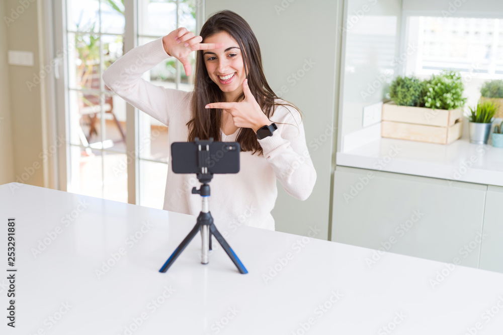 Beautiful young woman recording selfie video with smartphone webcam smiling making frame with hands and fingers with happy face. Creativity and photography concept. Beautiful young woman recording selfie video with smartphone webcam smiling making frame with hands and fingers with happy face. Creativity and photography concept.