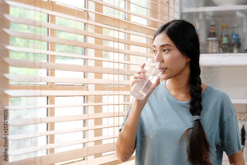 Youn beautiful asian woman drinking water while standing by window in kitchen background, peolpe and healthy lifestyles