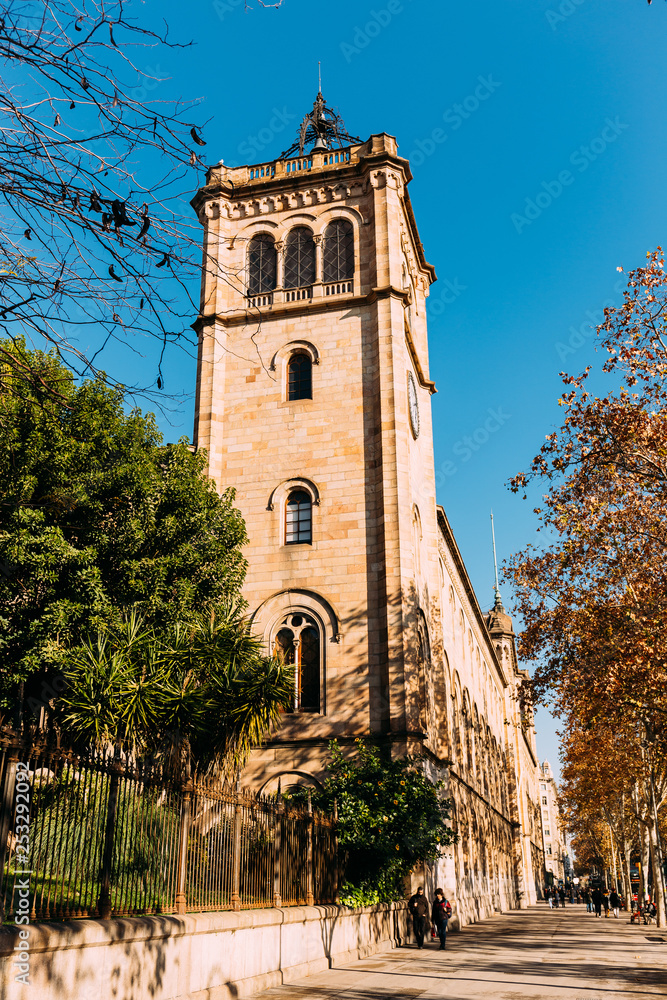BARCELONA, SPAIN - DECEMBER 28, 2018: street with green trees and high old tower on blue sky background