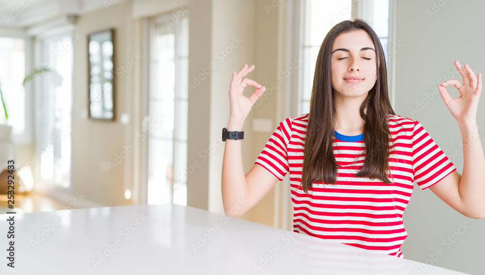 Beautiful young woman wearing casual stripes t-shirt relax and smiling with eyes closed doing meditation gesture with fingers. Yoga concept. Beautiful young woman wearing casual stripes t-shirt relax and smiling with eyes closed doing meditation gesture with fingers. Yoga concept.