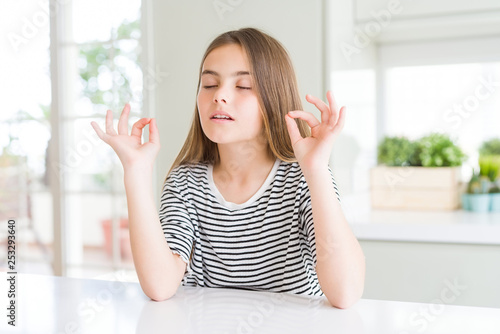 Beautiful young girl kid wearing stripes t-shirt relax and smiling with eyes closed doing meditation gesture with fingers. Yoga concept.