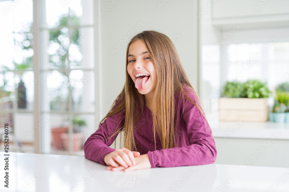 Beautiful young girl kid on white table sticking tongue out happy with funny expression. Emotion concept. Beautiful young girl kid on white table sticking tongue out happy with funny expression. Emotion concept.