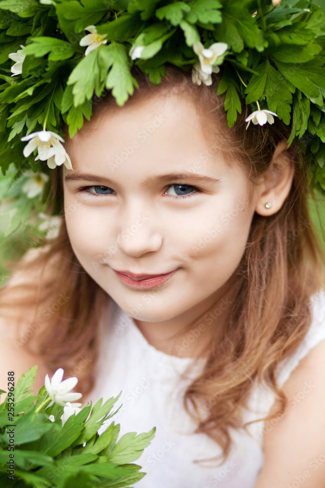 Beautiful little girl in a white dress in the spring wood. Portrait of the pretty little girl with a wreath from spring flowers on the head. Easter time Beautiful little girl in a white dress in the spring wood. Portrait of the pretty little girl with a wreath from spring flowers on the head. Easter time