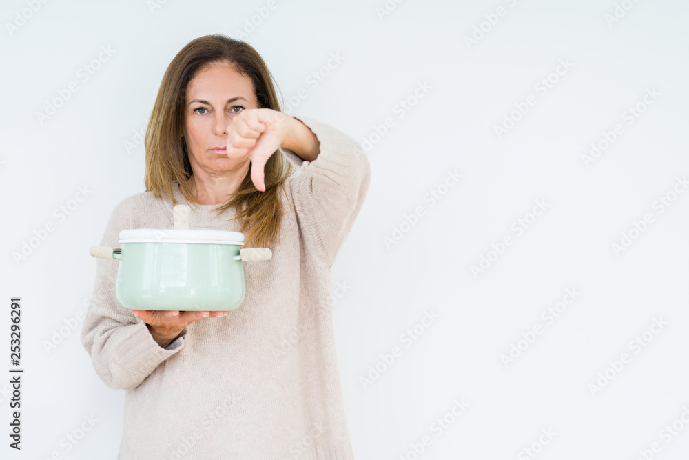 Middle age housewife woman holding iron cooking pot over isolated background with angry face, negative sign showing dislike with thumbs down, rejection concept Middle age housewife woman holding iron cooking pot over isolated background with angry face, negative sign showing dislike with thumbs down, rejection concept