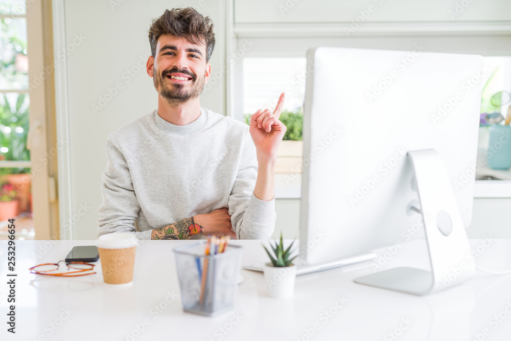 Young man working using computer with a big smile on face, pointing with hand and finger to the side looking at the camera. Young man working using computer with a big smile on face, pointing with hand and finger to the side looking at the camera.