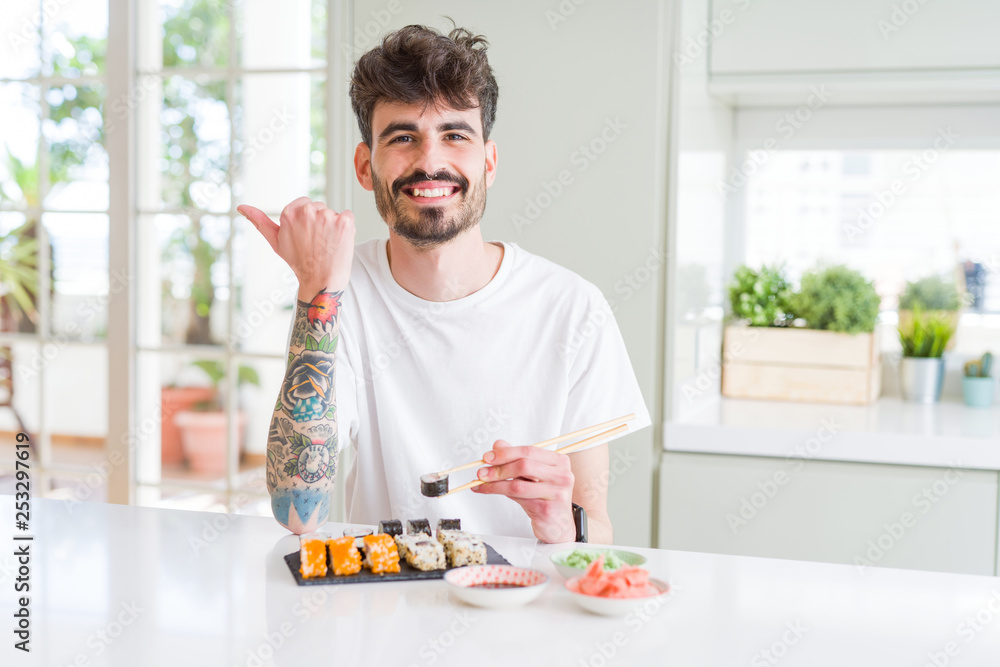 Young man eating asian sushi from home delivery pointing and showing with thumb up to the side with happy face smiling Young man eating asian sushi from home delivery pointing and showing with thumb up to the side with happy face smiling